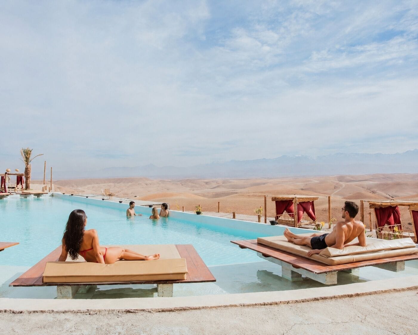 Una piscina con sillas de descanso, un paisaje desértico al fondo y un cielo despejado.