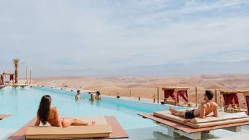 Una piscina con sillas de descanso, un paisaje desértico al fondo y un cielo despejado.