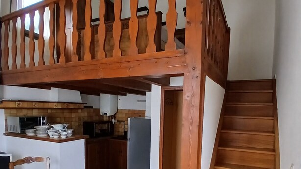 A spacious kitchen with a dining area, wooden staircase, and a view of the upper floor.
