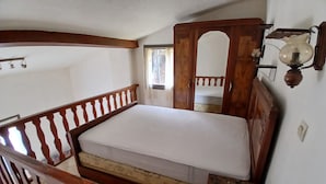 A bedroom with a wooden bed, a small bedside table, a wooden railing, and a wall-mounted light fixture.