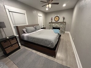 Een slaapkamer met een bed, nachtkastje, lamp, kast, vloerkleed, open haard en een klok aan de muur.