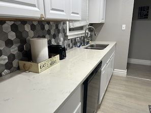 Een keuken met witte kastjes, een roestvrijstalen spoelbak, een magnetron en een backsplash van hexagontegels.