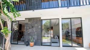 Una casa moderna con pared de piedra, puertas correderas de vidrio amplias y un área de estar exterior visible.