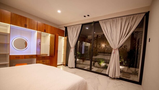 Un dormitorio moderno con cama, armarios de madera, un espejo circular y una puerta corredera de vidrio que da a un jardín.