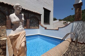 A statue near a swimming pool with stone walls and a tiled floor. - 1095 Casa Nido del Buho (Cómpeta)