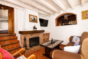 A living room with a fireplace, a television mounted on the wall, and a staircase leading to another room. - 1095 Casa Nido del Buho (Cómpeta)