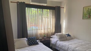 Ein Zimmer mit zwei Betten, einem Vorhangfenster, einer Lampe und einer Wanddekoration.
