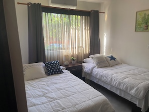 Ein Zimmer mit zwei Betten, einem Vorhangfenster, einer Lampe und einer Wanddekoration.