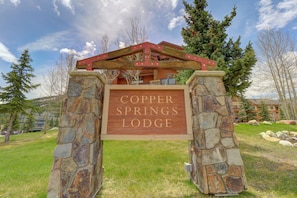 Ein hölzernes Schild mit der Aufschrift "Copper Springs Lodge", gestützt von Steinpfeilern, mit einem Gebäude im Hintergrund.