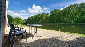 A gravel patio with a table and chairs, a view of a lake, and a forested area. - Holiday Home in Amstelveen With Terrace (Amstelveen)