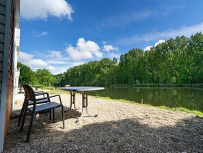 Een terras met grind, een tafel en stoelen, met uitzicht op een meer en een bebost gebied.