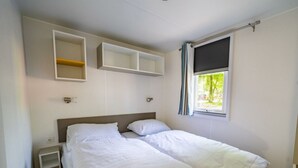A bedroom with a bed, a nightstand, built-in shelving, a window with curtains, and a view of greenery outside. - Holiday Home in Amstelveen With Terrace (Amstelveen)