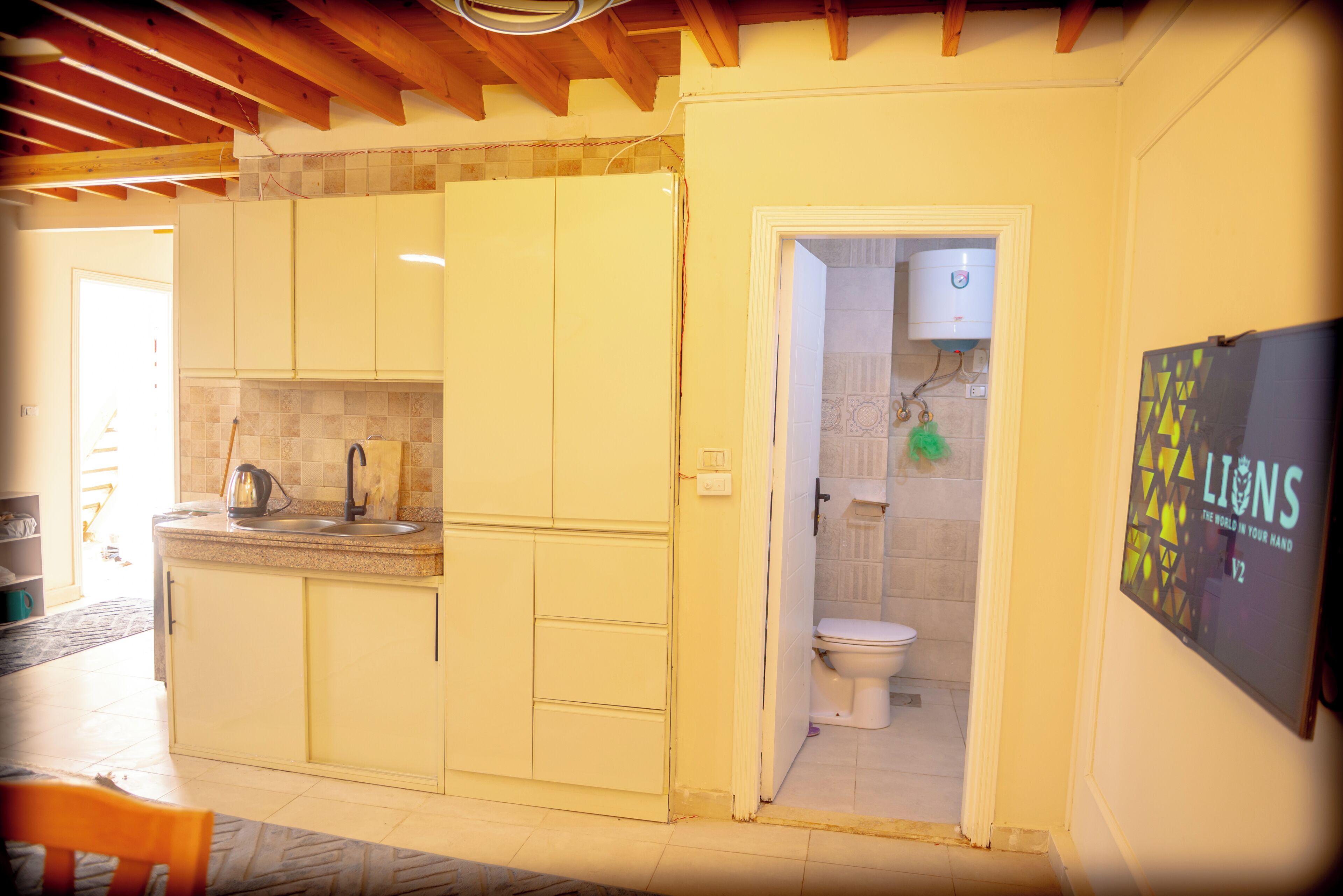 Cocina compacta con lavamanos, alacenas y una puerta que da a un baño con inodoro y ducha.