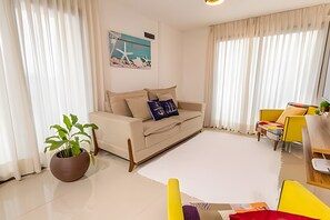 Una sala de estar con un sofá color beige, un sillón amarillo, una planta en maceta y un cuadro en la pared.