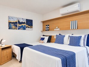 A hotel room with two beds, a nightstand, a desk, and a wall-mounted air conditioner.