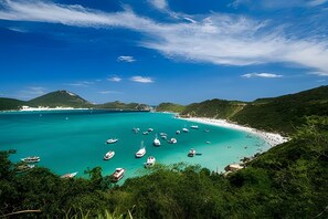 Ett kustlandskap med båtar som ligger ankrade nära en strand, omgivet av grönska och kullar.