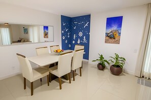 Un comedor con una mesa blanca, cuatro sillas, un frutero, una pared azul con motivos náuticos, dos plantas en macetas y un cuadro en la pared.