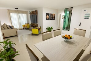 Ein modernes Wohnzimmer mit einer Couch, einem Esstisch mit Obst und einem Fernseher.