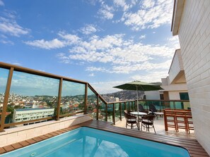 A rooftop pool area with a view of a cityscape, outdoor seating, and a clear sky.