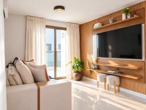 A modern living room with a sofa, a flat-screen TV, a potted plant, and a wooden wall paneling.