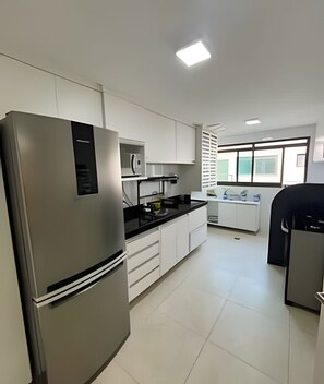 A modern kitchen with stainless steel appliances, white cabinetry, and a large window providing natural light.