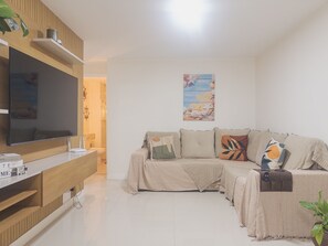 Ein modernes Wohnzimmer mit Flachbildfernseher, einer Holz-Unterhaltungsecke, einem beigen Sofa mit gemusterten Kissen und einer Wandablage mit Dekoration.