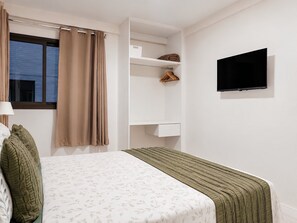 Una camera da letto con un letto, una televisione, un armadio e una finestra con tende.
