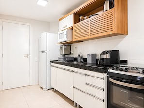 A compact kitchen with white cabinetry, a built-in oven, a microwave, and a coffee maker.