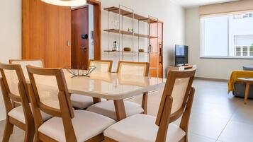 A dining area with a glass-top table, wooden chairs with woven seats, a bookshelf, and a television on a stand.
