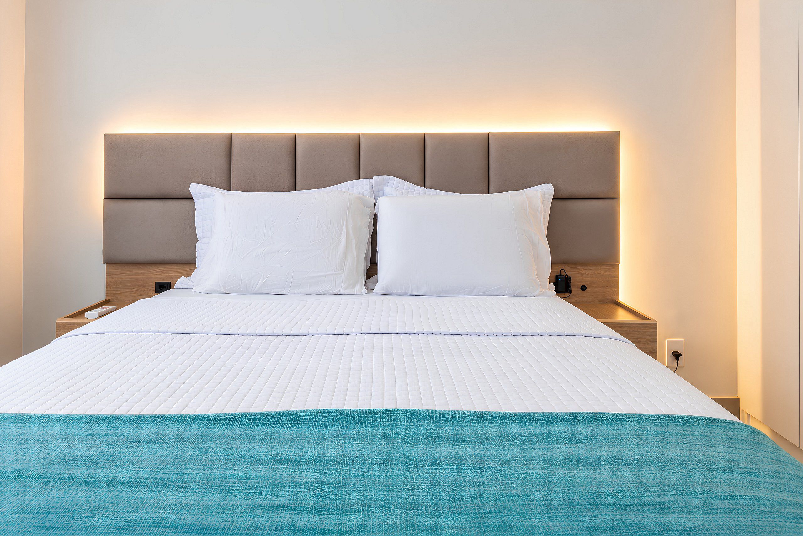A hotel room with a bed, a headboard, a nightstand, and a bedside table.