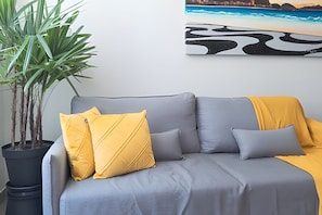 A grey sofa with yellow cushions, a potted plant, and a cityscape painting on the wall.