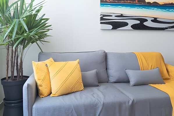 A grey sofa with yellow cushions, a potted plant, and a cityscape painting on the wall.