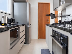 A modern kitchen with stainless steel appliances, a wooden door, and a tiled backsplash.