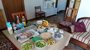 A dining table with food and drinks, a sofa, and chairs in a room with a tiled floor. - Casa Raffaella (Polignano a Mare)