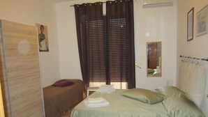 A bedroom with a bed, a chair, a wardrobe, and a window with curtains. - Casa Raffaella (Polignano a Mare)