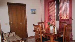 A dining area with a wooden table, four chairs, a sofa, and a window with a decorative screen. - Casa Raffaella (Polignano a Mare)