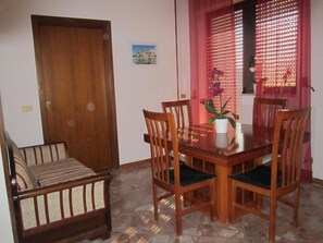 A dining area with a wooden table, four chairs, a sofa, and a window with a decorative screen.