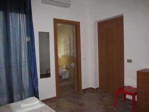 A room with a bed, a wooden door, a red stool, and a mirror on the wall. - Casa Raffaella (Polignano a Mare)