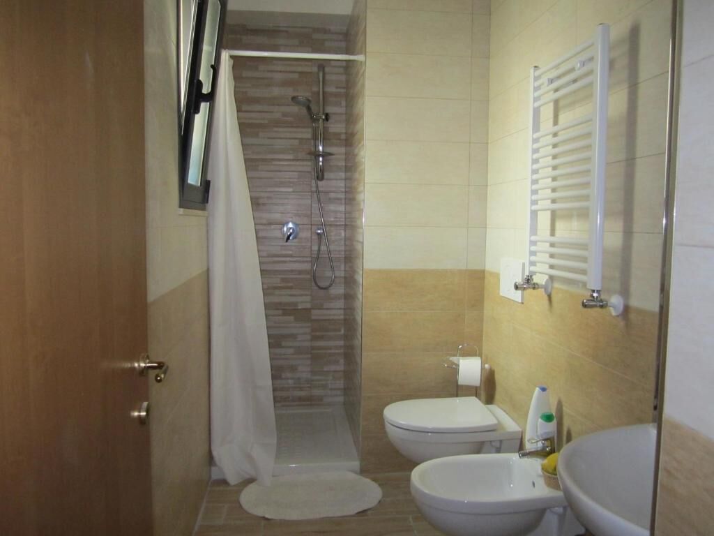 Un bagno con doccia, due servizi igienici, un lavandino e un portasciugamani.