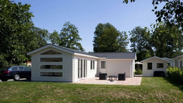 Ein weißes Gebäude mit überdachter Terrasse, ein Auto davor und ein kleines Wasserelement.