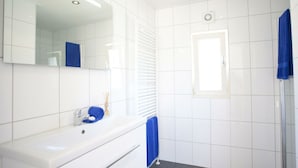 Ein modernes Badezimmer mit weißen Fliesen, einem großen Spiegel, einem Waschbecken, einem blauen Handtuch und einer Duschkabine.