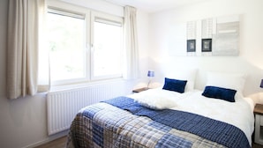 Ein Schlafzimmer mit Bett, Fenster, Heizkörper und einem Wandbild.