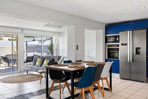 A modern kitchen with a built-in oven and refrigerator, a dining table with chairs, and a view to a patio area.