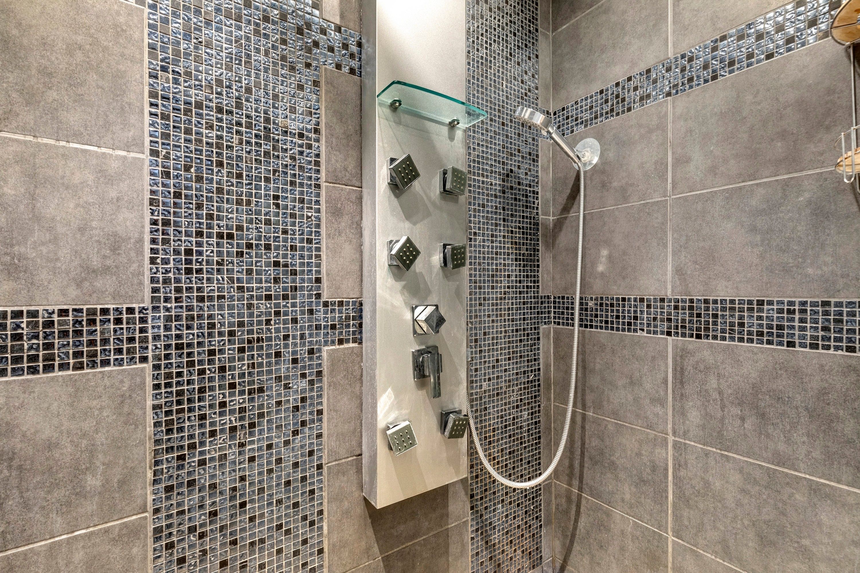 Un espace douche doté d’une étagère en verre, de plusieurs pommes de douche et de murs carrelés.
