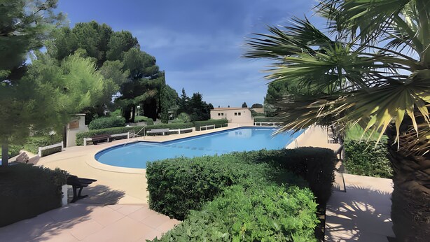 Une piscine entourée de verdure, un banc et un bâtiment en arrière-plan.