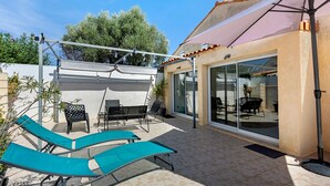 Une terrasse avec deux fauteuils, une table et une porte vitrée donnant sur un espace intérieur.