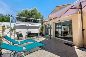 A patio area with a glass door leading to a room, outdoor seating with chairs and a table, and a pergola with hanging lights.