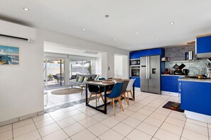 A modern kitchen with blue cabinets, a stainless steel refrigerator, and a dining area with a table and chairs.