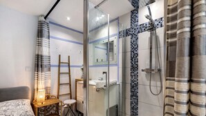 Une salle de bain moderne avec une douche à parois de verre, une petite table de chevet et un lit recouvert d’une couvre-lit à motifs.