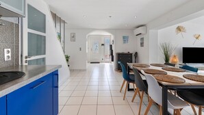 Une cuisine moderne avec des meubles bleus, un coin repas avec une table et des chaises en bois, et un téléviseur fixé au mur.